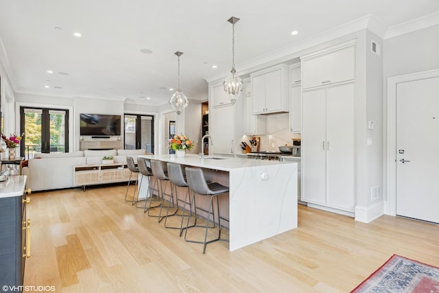 kitchen featuring a breakfast bar, a kitchen island with sink, hanging light fixtures, light wood-type flooring, and white cabinetry