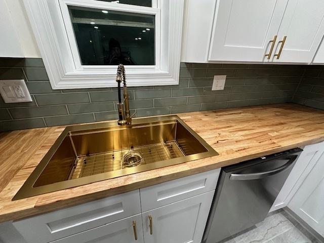 kitchen with wood counters, white cabinets, sink, stainless steel dishwasher, and tasteful backsplash