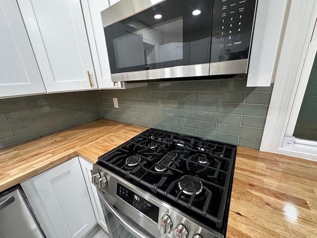 kitchen featuring tasteful backsplash, white cabinetry, stainless steel appliances, and wood counters