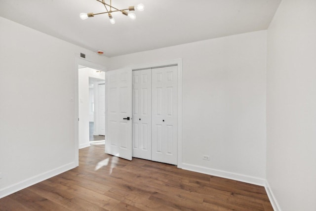 unfurnished bedroom with a closet, dark hardwood / wood-style flooring, and a notable chandelier