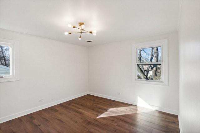 empty room featuring a notable chandelier, dark hardwood / wood-style floors, a healthy amount of sunlight, and ornamental molding