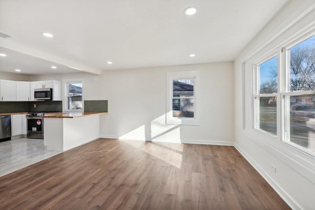 kitchen featuring white cabinets, kitchen peninsula, hardwood / wood-style floors, and appliances with stainless steel finishes