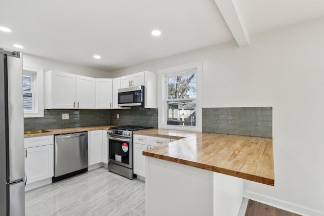 kitchen featuring butcher block countertops, white cabinets, kitchen peninsula, and stainless steel appliances