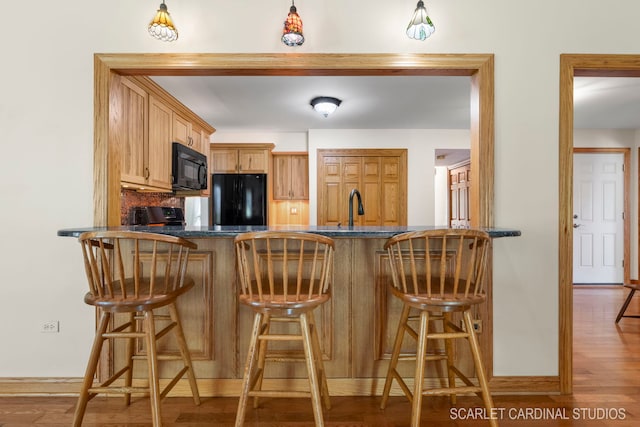 kitchen with black appliances, hanging light fixtures, kitchen peninsula, a breakfast bar, and hardwood / wood-style flooring