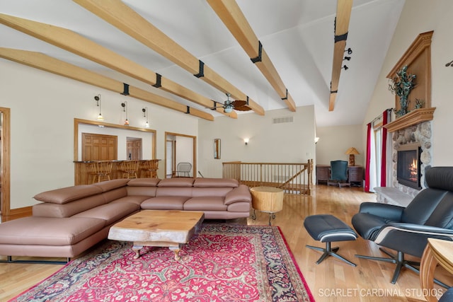 living room featuring light wood-type flooring, beam ceiling, ceiling fan, and a stone fireplace