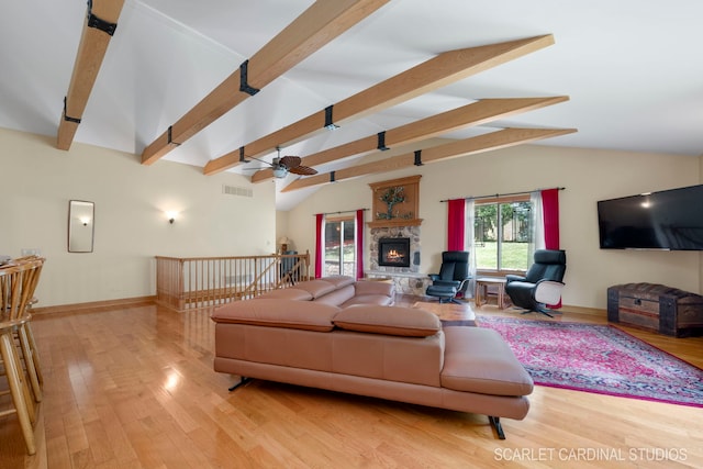 living room featuring lofted ceiling with beams, ceiling fan, light wood-type flooring, and a stone fireplace