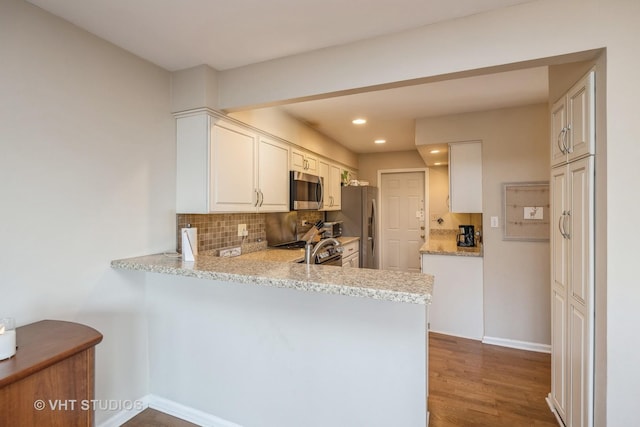 kitchen featuring dark wood-type flooring, white cabinetry, light stone counters, kitchen peninsula, and stainless steel appliances