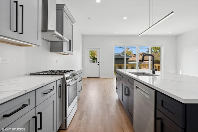 kitchen with gray cabinetry, light stone countertops, sink, wall chimney range hood, and appliances with stainless steel finishes