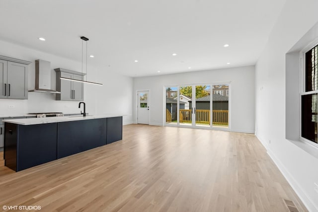 kitchen featuring gray cabinets, sink, wall chimney range hood, and light wood-type flooring