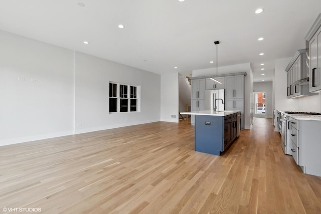 kitchen featuring light wood-type flooring, stainless steel appliances, sink, gray cabinets, and an island with sink