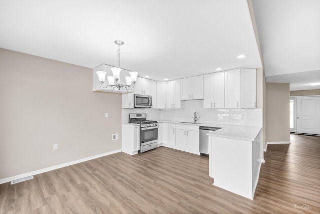 kitchen with stainless steel appliances, sink, light hardwood / wood-style floors, white cabinetry, and hanging light fixtures