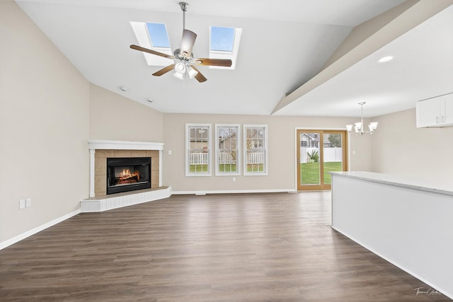 unfurnished living room featuring a tiled fireplace, lofted ceiling with skylight, dark hardwood / wood-style flooring, and ceiling fan with notable chandelier