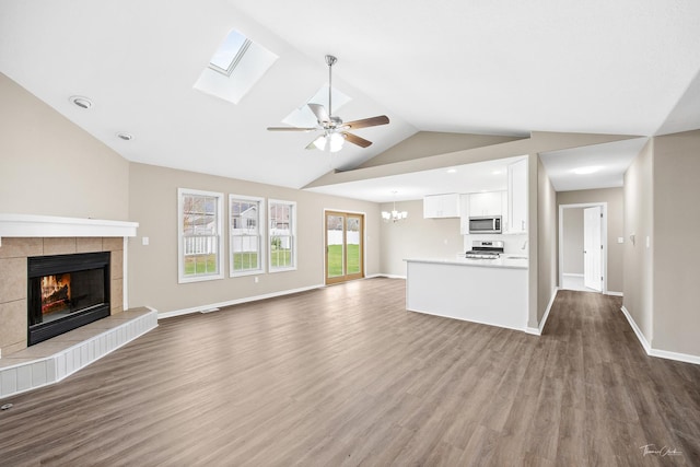 unfurnished living room featuring ceiling fan with notable chandelier, hardwood / wood-style flooring, lofted ceiling with skylight, and a tiled fireplace