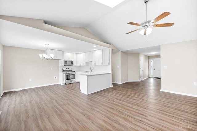 unfurnished living room featuring ceiling fan with notable chandelier, light wood-type flooring, sink, and vaulted ceiling