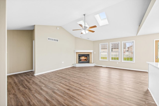 unfurnished living room featuring a fireplace, ceiling fan, vaulted ceiling with skylight, and hardwood / wood-style flooring