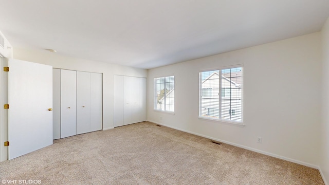 unfurnished bedroom featuring light carpet and two closets