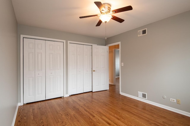 unfurnished bedroom featuring hardwood / wood-style floors, ceiling fan, and multiple closets