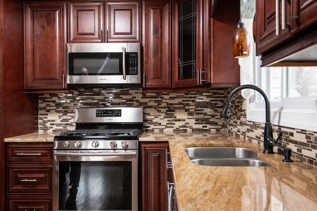 kitchen featuring backsplash, light stone countertops, sink, and appliances with stainless steel finishes