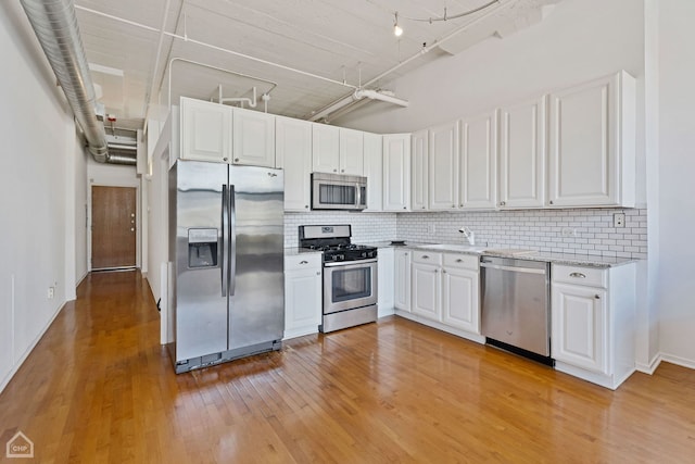 kitchen with white cabinets, decorative backsplash, appliances with stainless steel finishes, and light hardwood / wood-style flooring