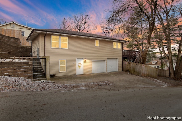 back house at dusk with a garage and a wooden deck