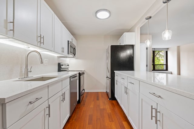 kitchen with stainless steel appliances, sink, pendant lighting, dark hardwood / wood-style floors, and white cabinetry