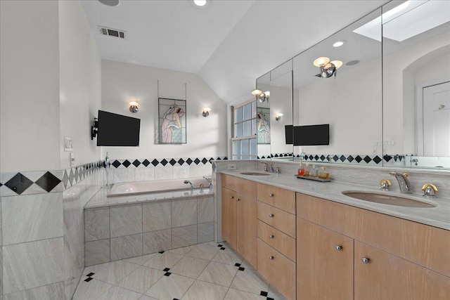 bathroom featuring tiled tub, lofted ceiling with skylight, tile patterned flooring, and vanity