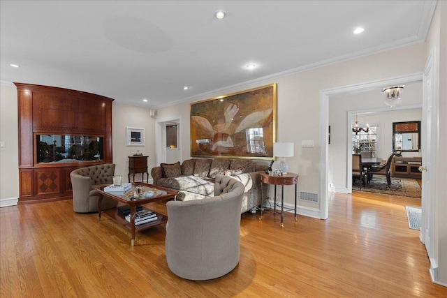 living room with crown molding, a chandelier, and light hardwood / wood-style floors