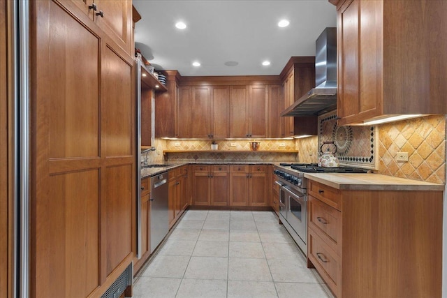 kitchen featuring sink, stainless steel appliances, wall chimney range hood, tasteful backsplash, and light tile patterned floors