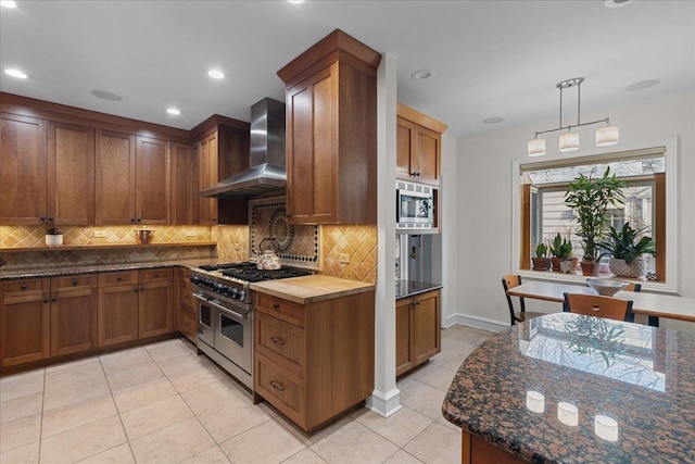 kitchen with decorative backsplash, stainless steel appliances, wall chimney range hood, light tile patterned floors, and hanging light fixtures