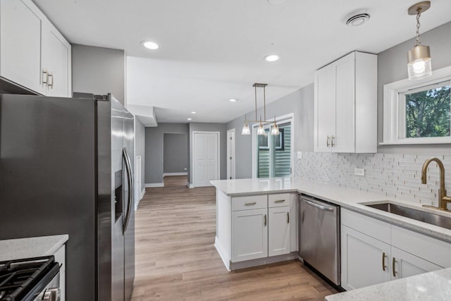 kitchen featuring kitchen peninsula, appliances with stainless steel finishes, sink, decorative light fixtures, and white cabinets