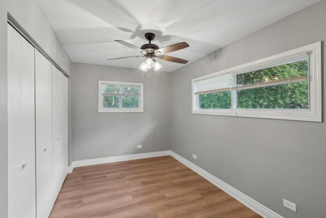 unfurnished bedroom with ceiling fan, light hardwood / wood-style floors, a closet, and multiple windows