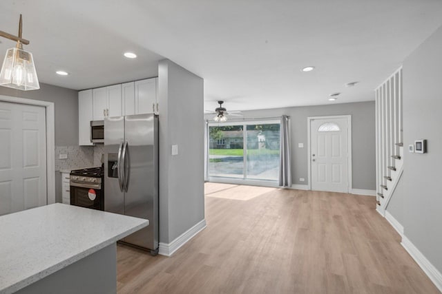 kitchen with white cabinetry, ceiling fan, backsplash, light hardwood / wood-style floors, and appliances with stainless steel finishes