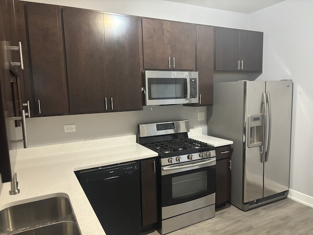 kitchen with appliances with stainless steel finishes, light hardwood / wood-style floors, dark brown cabinets, and sink