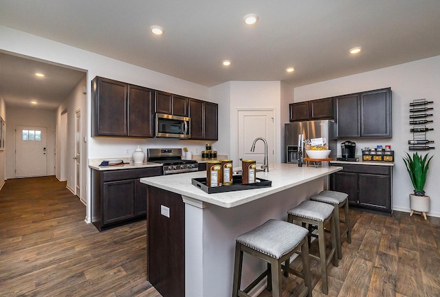 kitchen featuring dark hardwood / wood-style floors, stainless steel appliances, a breakfast bar area, and an island with sink