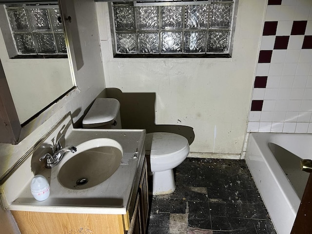 bathroom featuring vanity, a tub to relax in, and toilet