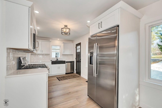 kitchen featuring appliances with stainless steel finishes, sink, white cabinets, decorative backsplash, and light hardwood / wood-style floors