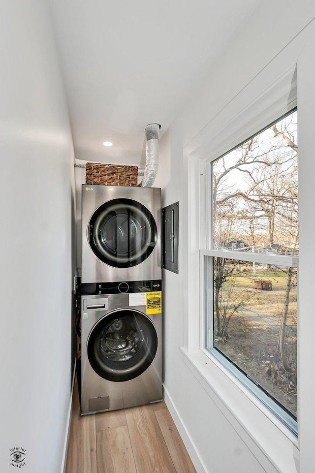 laundry room with light hardwood / wood-style floors, electric panel, and stacked washing maching and dryer