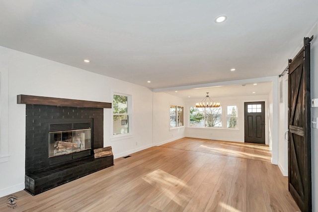 unfurnished living room featuring a brick fireplace, a barn door, a chandelier, and light wood-type flooring