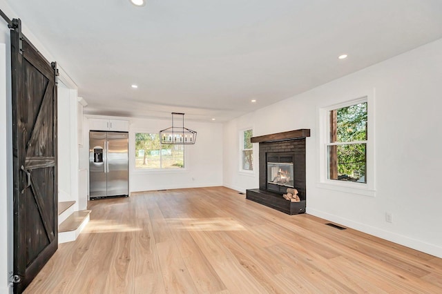 unfurnished living room with a fireplace, a barn door, and light wood-type flooring