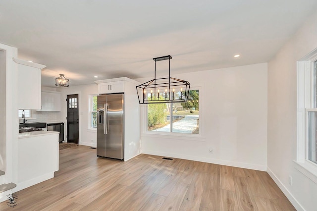 kitchen featuring pendant lighting, white cabinets, backsplash, stainless steel appliances, and light wood-type flooring