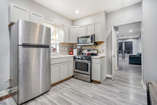 kitchen with white cabinets, decorative backsplash, stainless steel appliances, and light hardwood / wood-style flooring