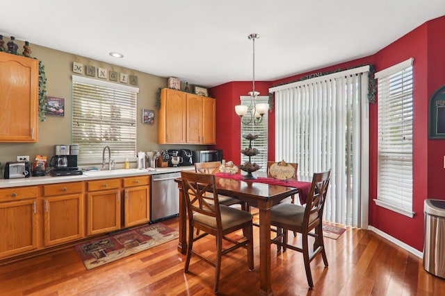 kitchen with stainless steel dishwasher, sink, wood-type flooring, decorative light fixtures, and a chandelier