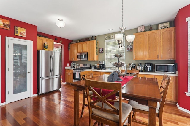 kitchen featuring appliances with stainless steel finishes, hardwood / wood-style flooring, an inviting chandelier, and pendant lighting