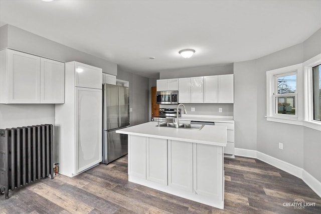 kitchen with radiator, sink, an island with sink, appliances with stainless steel finishes, and white cabinetry