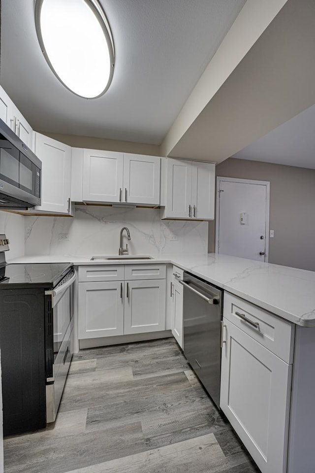 kitchen with sink, tasteful backsplash, kitchen peninsula, white cabinets, and appliances with stainless steel finishes