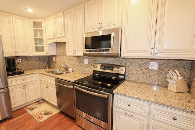 kitchen with hardwood / wood-style floors, sink, decorative backsplash, light stone counters, and stainless steel appliances