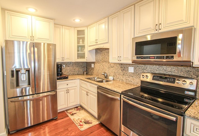 kitchen featuring sink, stainless steel appliances, tasteful backsplash, light stone counters, and hardwood / wood-style floors