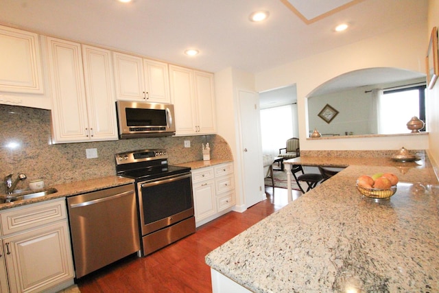 kitchen with backsplash, sink, dark hardwood / wood-style floors, light stone countertops, and stainless steel appliances