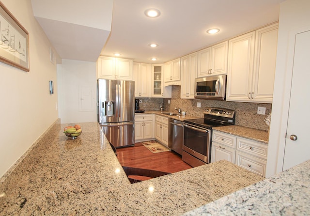 kitchen featuring light stone countertops, appliances with stainless steel finishes, decorative backsplash, sink, and dark hardwood / wood-style floors