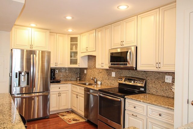 kitchen with decorative backsplash, light stone counters, stainless steel appliances, dark wood-type flooring, and sink